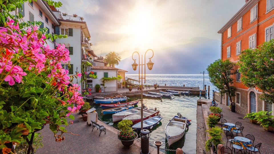 A waterfront with boats docked, a street with cafes, and buildings with balconies.