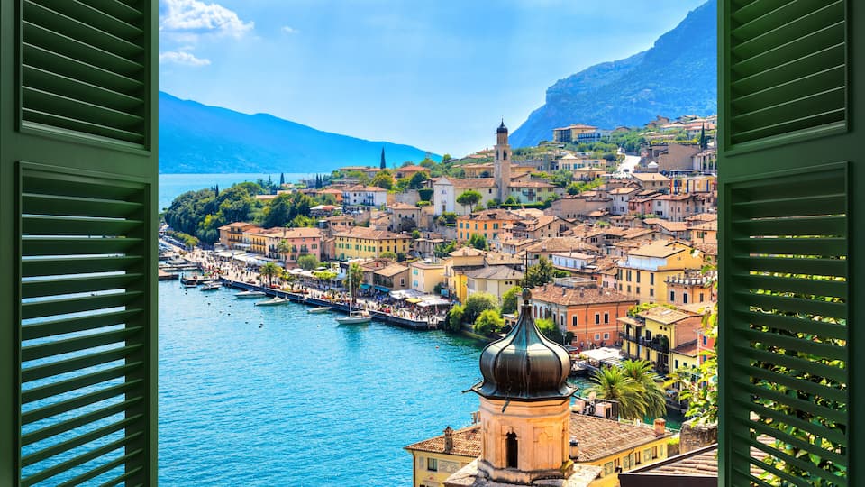 A coastal town with a prominent tower, a river, and mountains in the background.