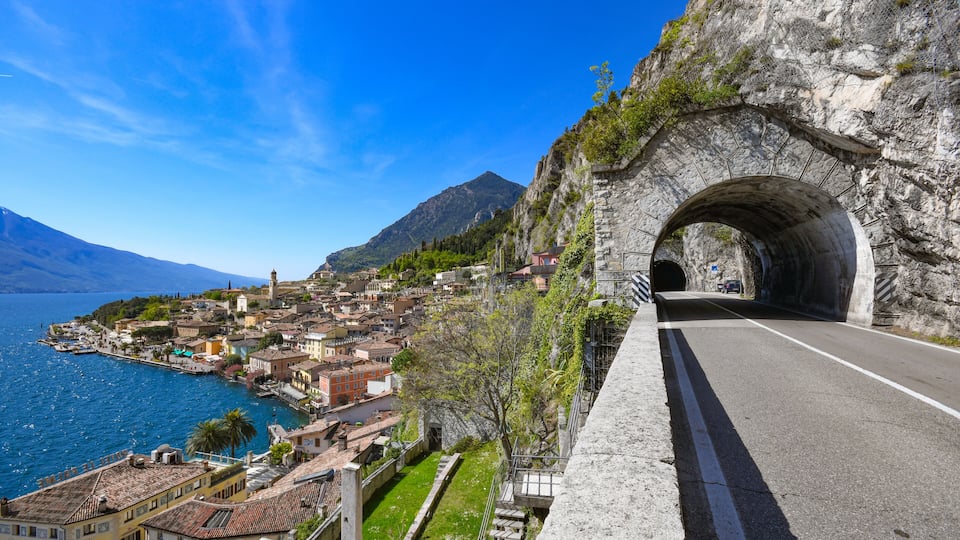 A coastal town with a stone bridge, a clear blue sky, and a mountain in the background.