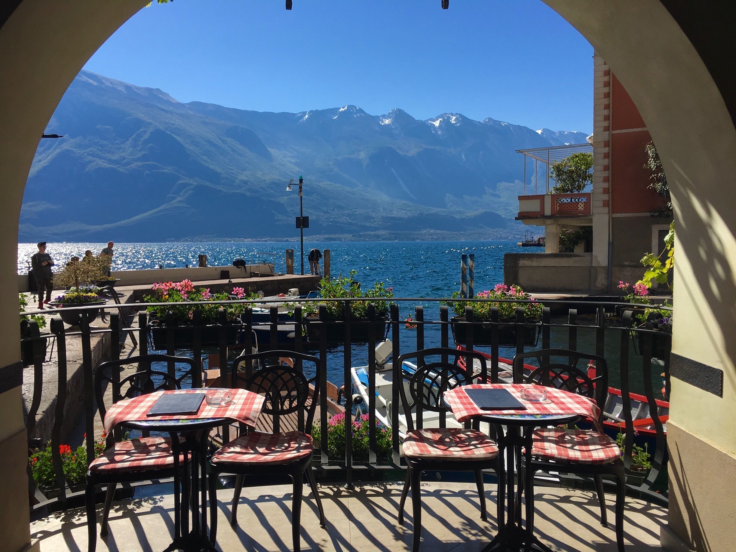 A terrace with tables and chairs overlooking a body of water with mountains in the background.