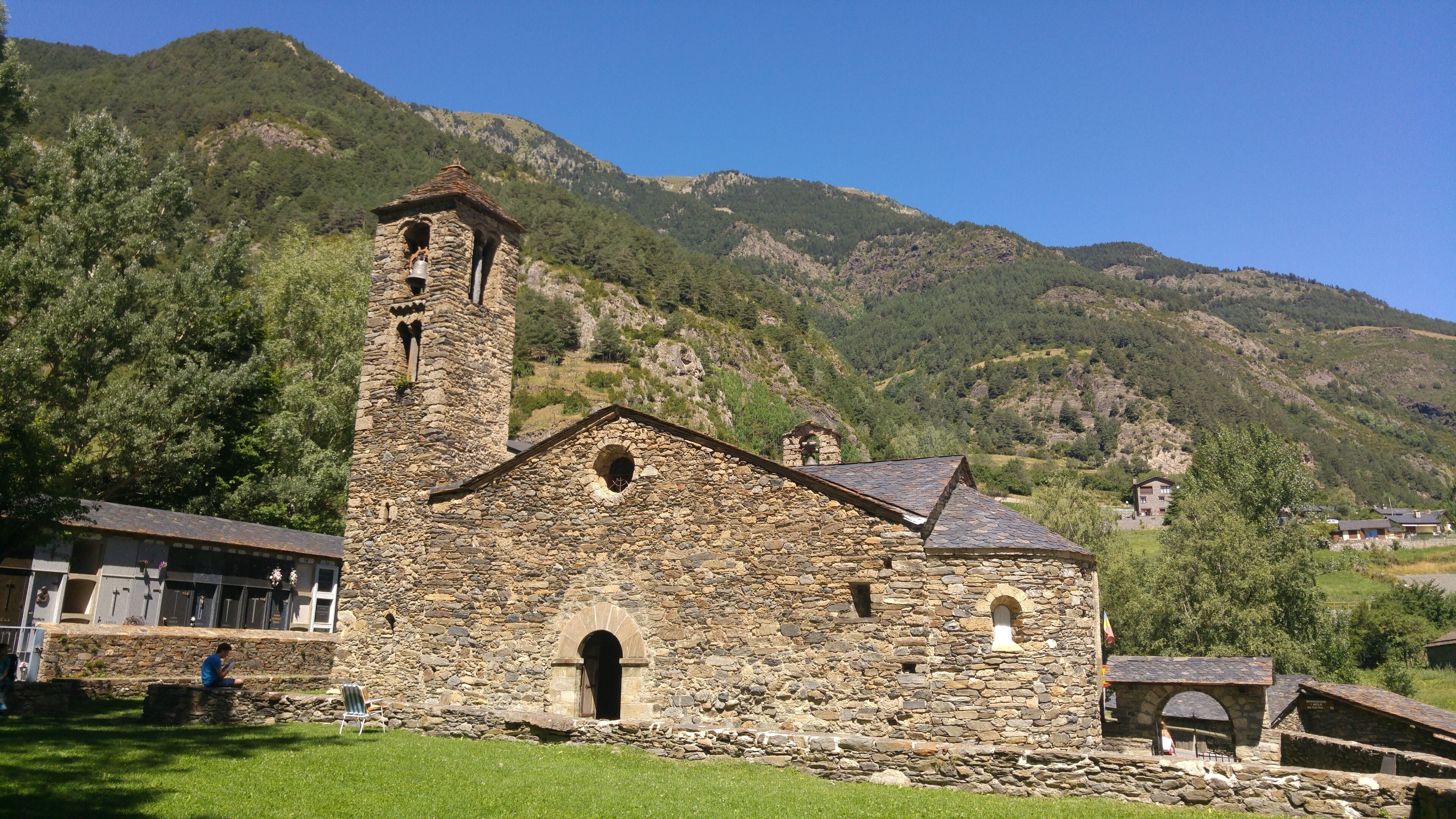 A stone church with a bell tower, surrounded by lush green hills and mountains.