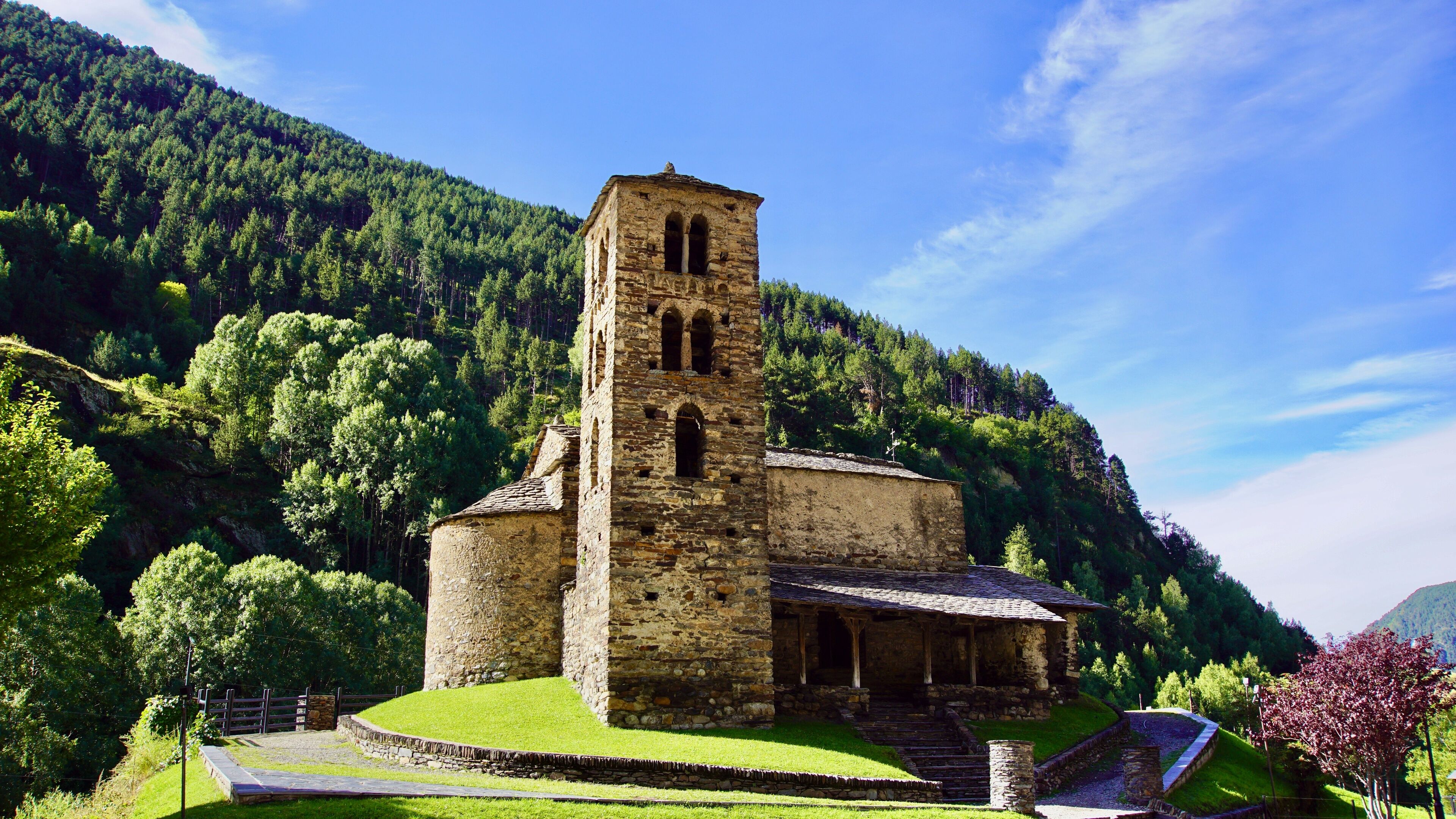A stone church with a bell tower surrounded by lush green forest and hills.