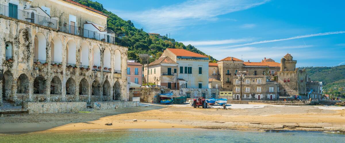 A coastal town with clear waters, historic buildings, and a sandy beach.