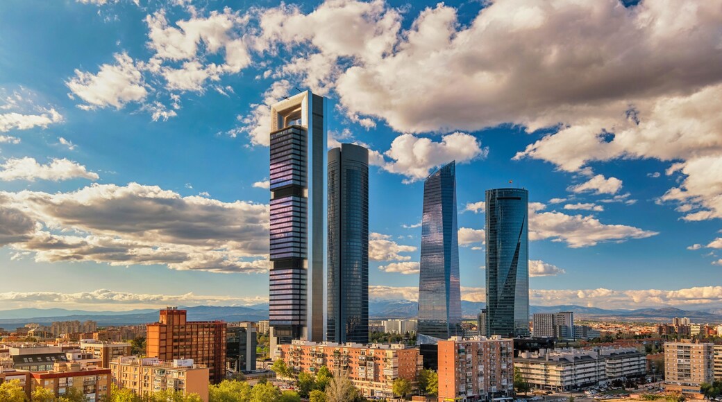 Un paisaje urbano con rascacielos modernos y montañas al fondo, bajo un cielo parcialmente nublado.