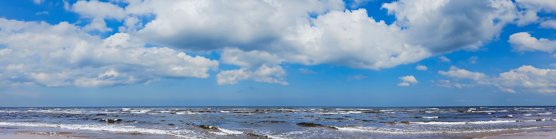 Una playa con olas, una orilla arenosa y un cielo parcialmente nublado.