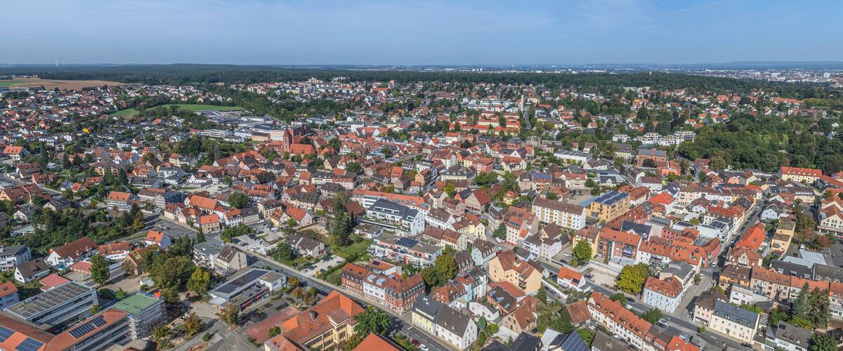 An aerial view of a densely populated town with red-roofed houses, a prominent church, and green spaces.
