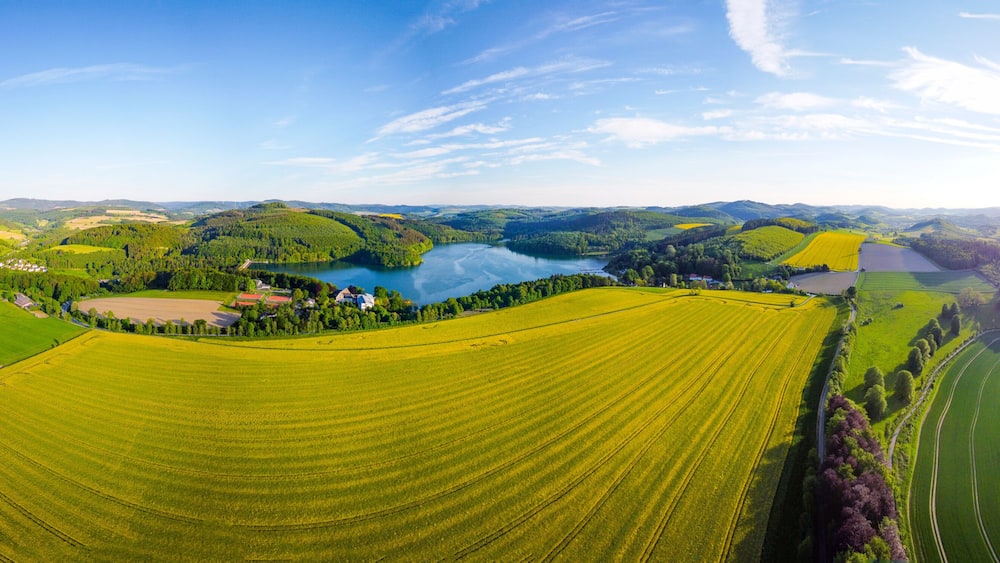A panoramic view of a rural landscape with a lake, fields, and a small village.