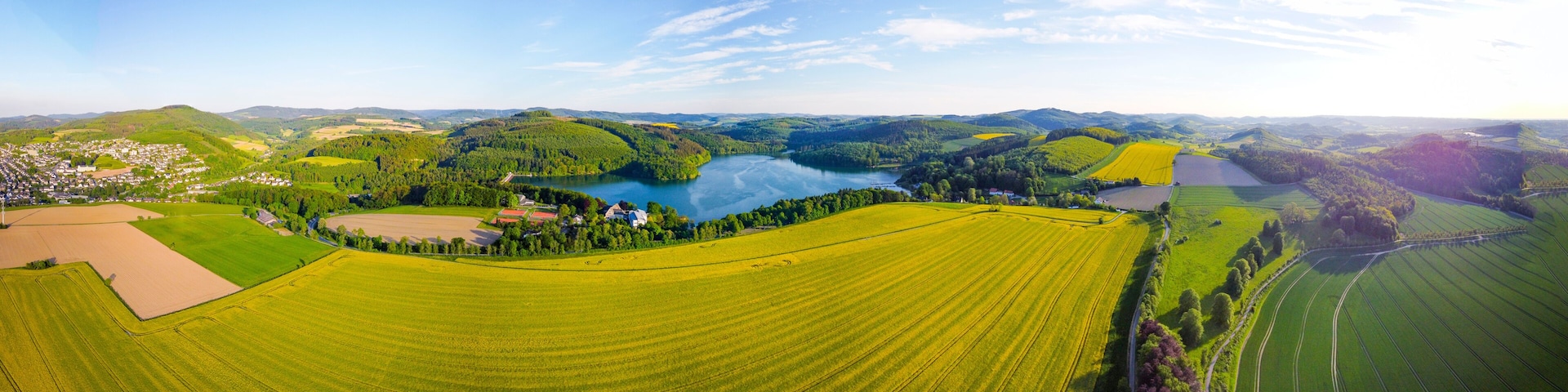 A panoramic view of a rural landscape with a lake, fields, and a small village.