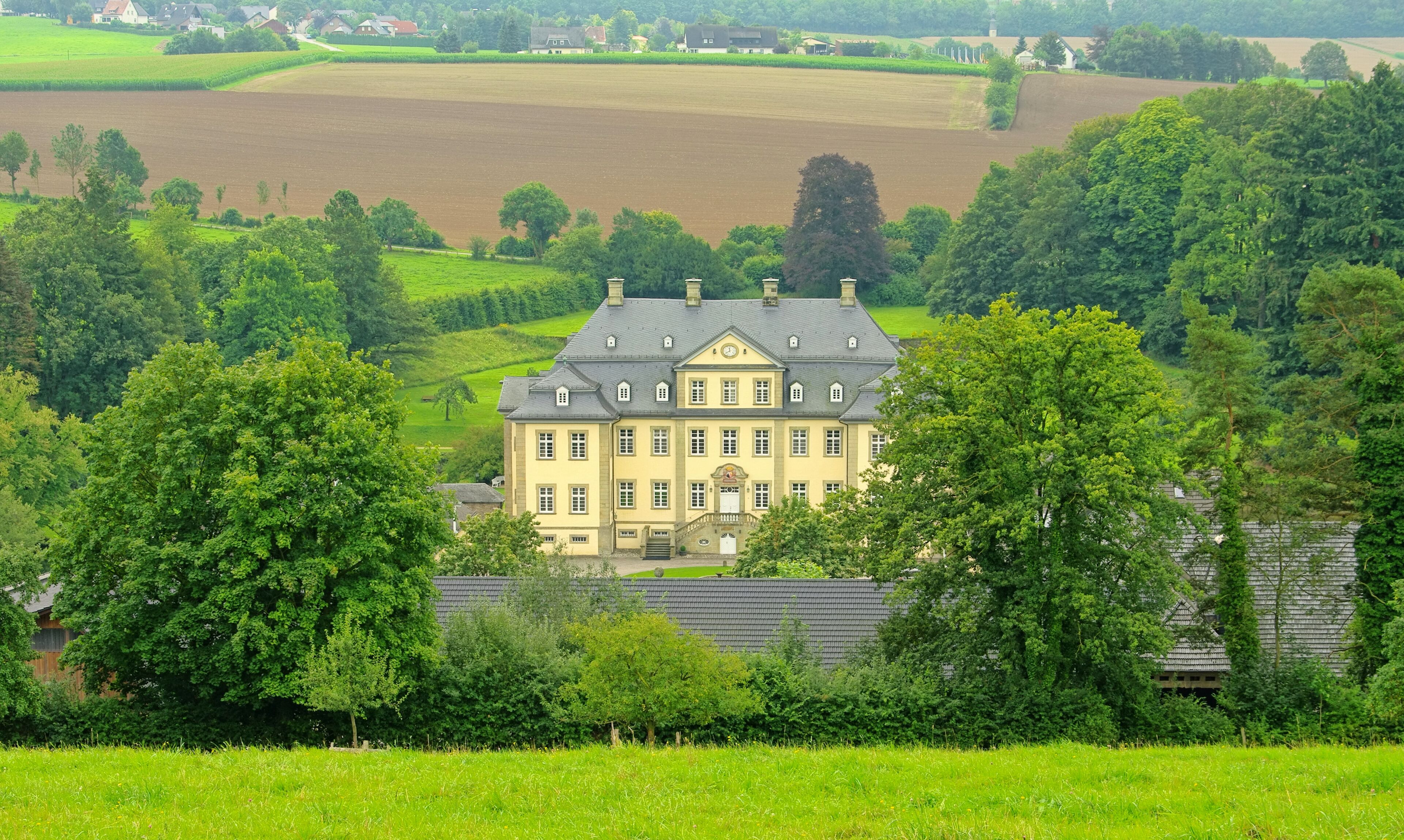 A large, historic house surrounded by lush green fields and trees.