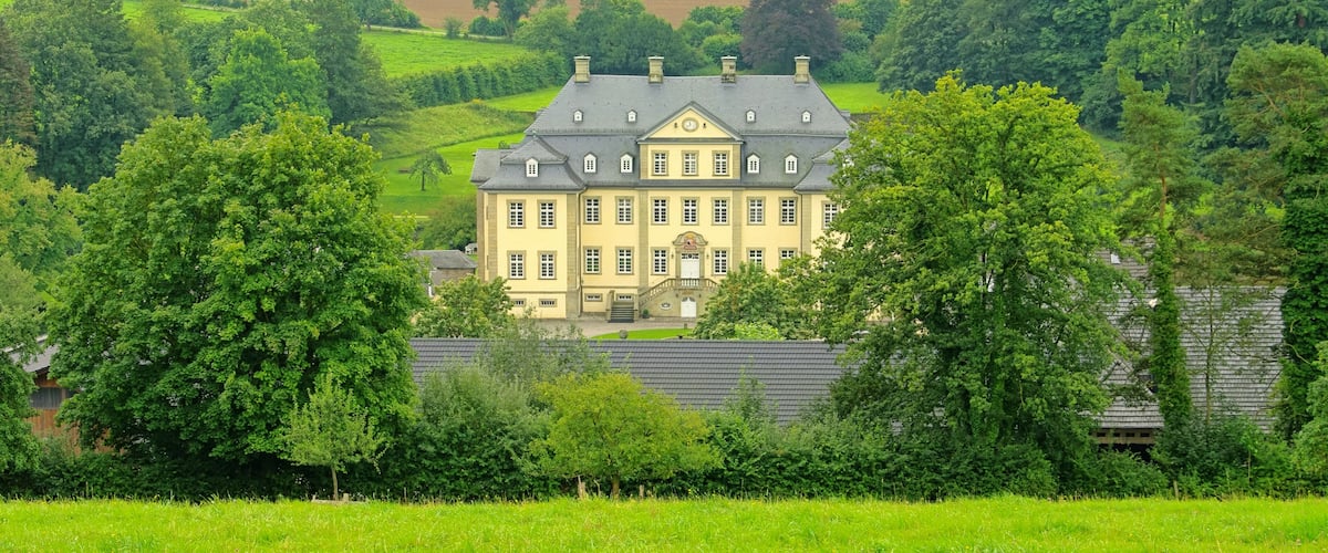 A large, historic house surrounded by lush green fields and trees.