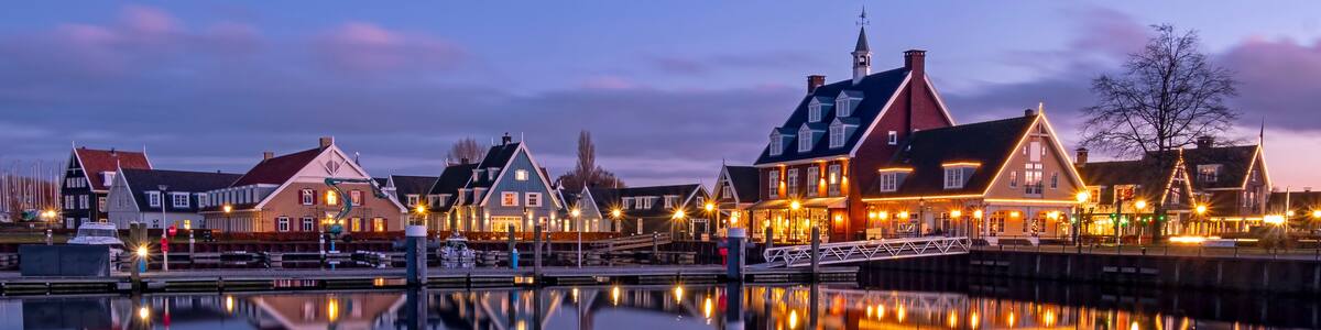 A waterfront town with traditional houses, a calm river, and a bridge reflecting the buildings.