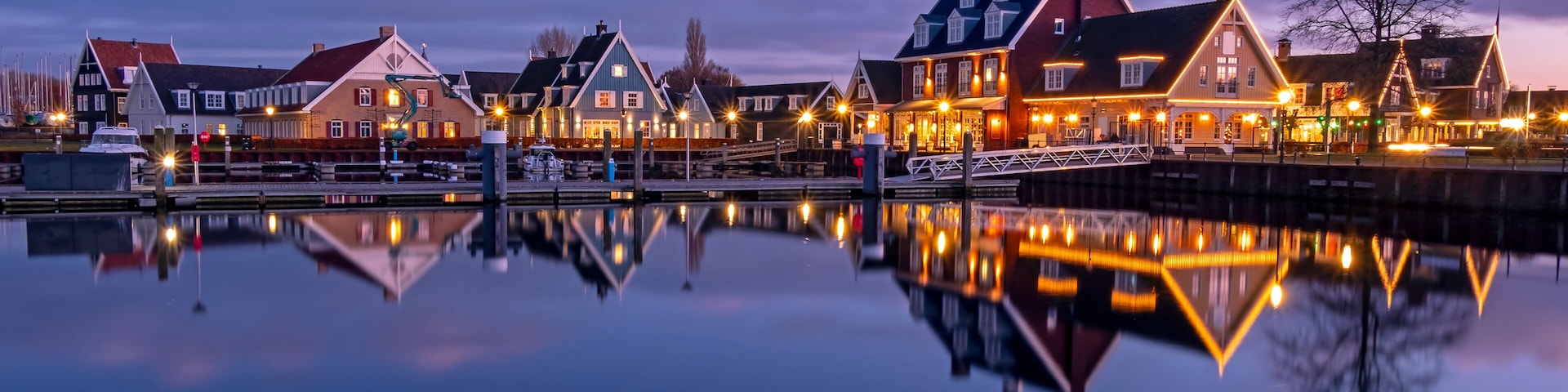 Un pueblo en la costa con casas tradicionales, un río tranquilo y un puente que refleja los edificios.