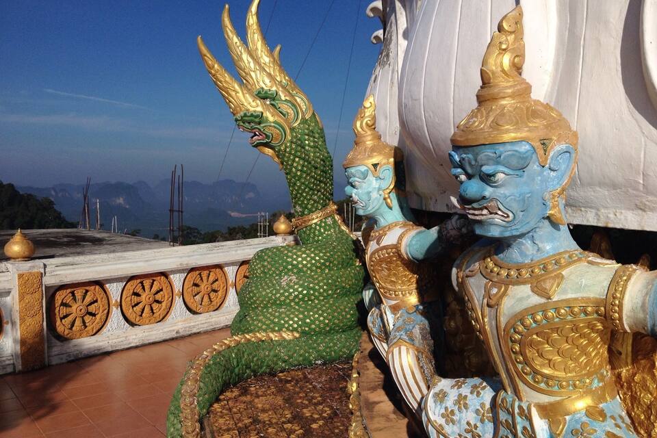 A green and gold dragon statue and a blue and gold figure on a rooftop with a mountainous backdrop.