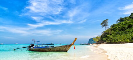 Ein Strand mit klarem türkisblauem Wasser, einem hölzernen Boot und einem sandigen Ufer mit Bäumen.