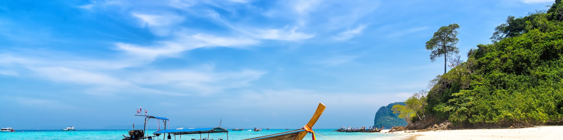 A beach with clear turquoise waters, a wooden boat, and a sandy shore with trees.