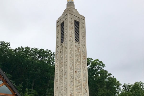 Ein hoher, steinerner Turm mit einer Statue auf der Spitze.