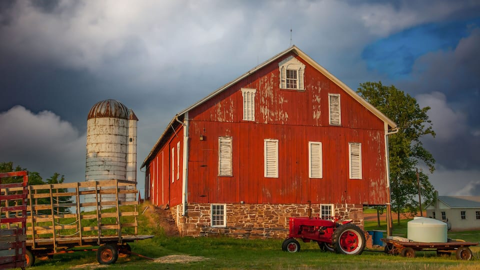 A red barn with a silo, a red tractor, and a white water tank.