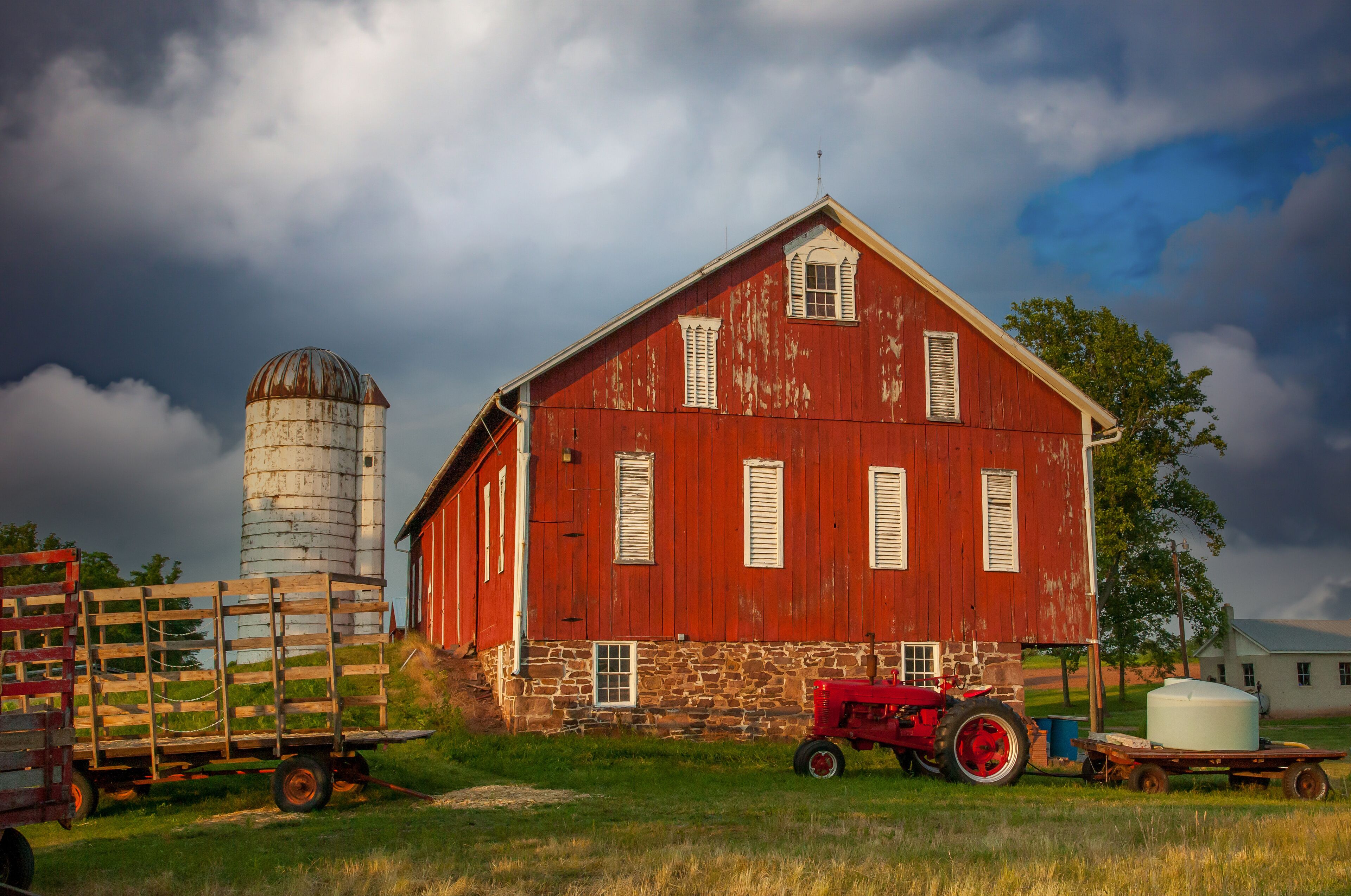 A red barn with a silo, a red tractor, and a white water tank.