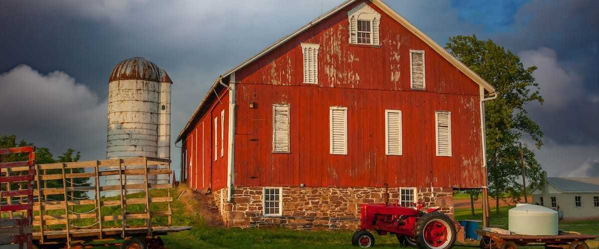 A red barn with a silo, a red tractor, and a white water tank.