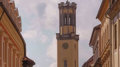 Una torre histórica con un reloj, rodeada de arquitectura europea clásica.