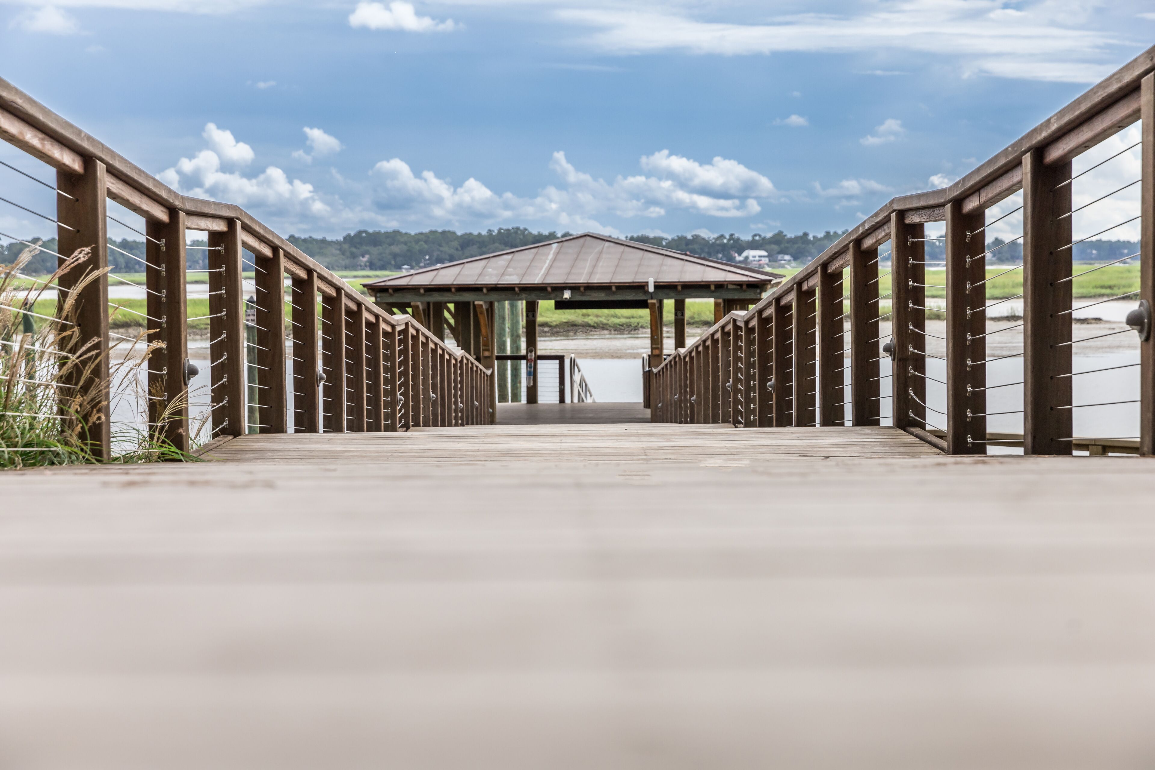 Un puente de madera que conduce a un pabellón sobre el agua, rodeado de follaje.