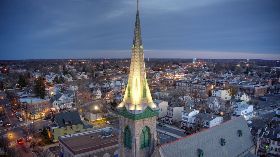 A cityscape at dusk with a prominent church spire illuminated against a twilight sky.