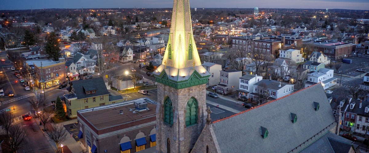 A cityscape at dusk with a prominent church spire illuminated against a twilight sky.