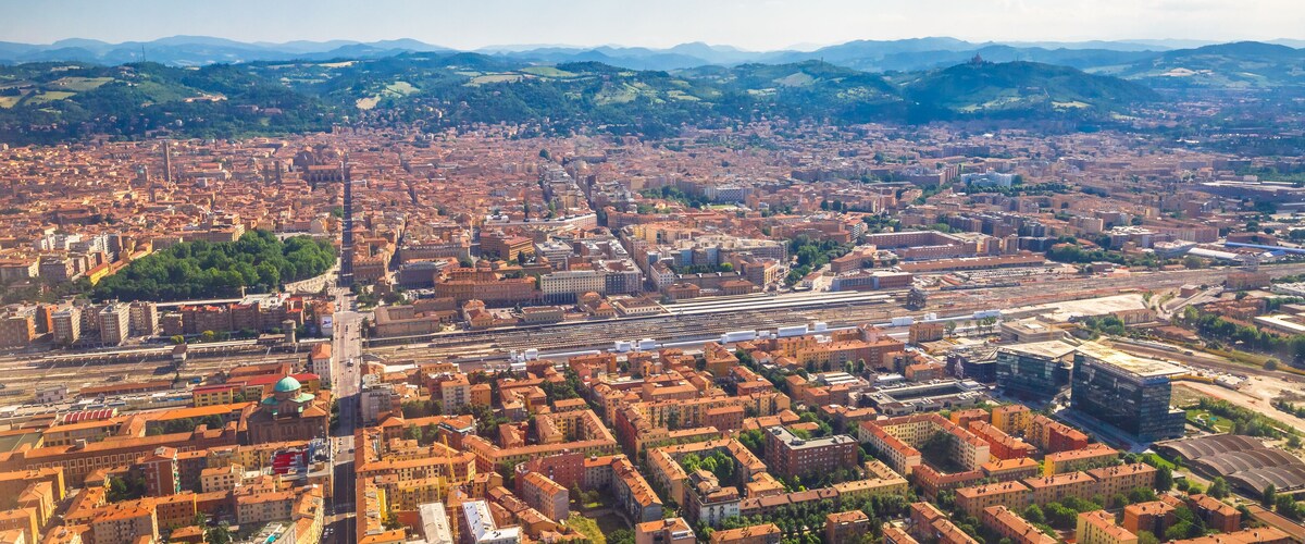 Vista aérea de una ciudad con arquitectura urbana densa, una torre central destacada y colinas verdes circundantes.