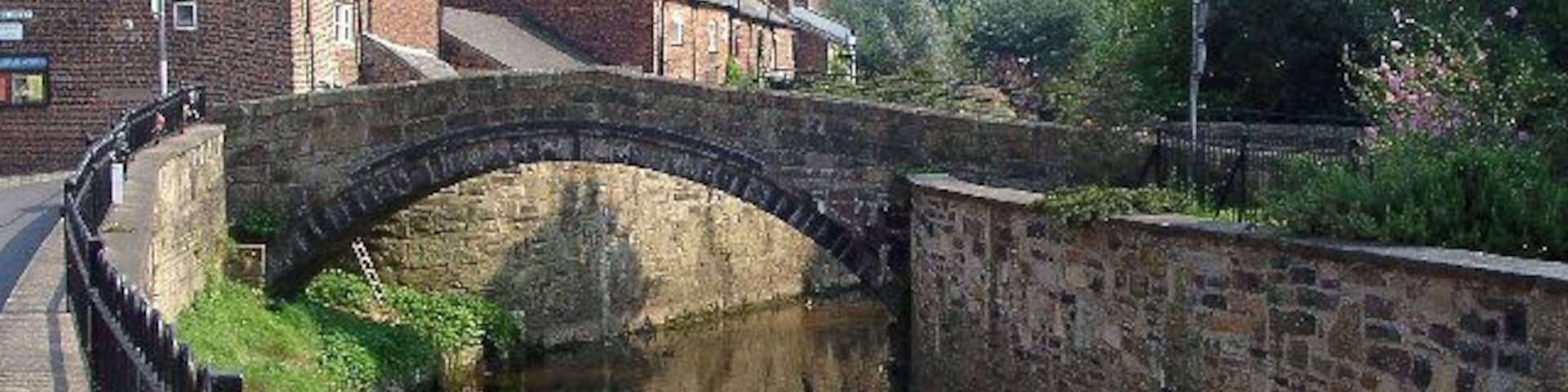 Un puente de piedra sobre un canal, con edificios de ladrillo y una iglesia al fondo.