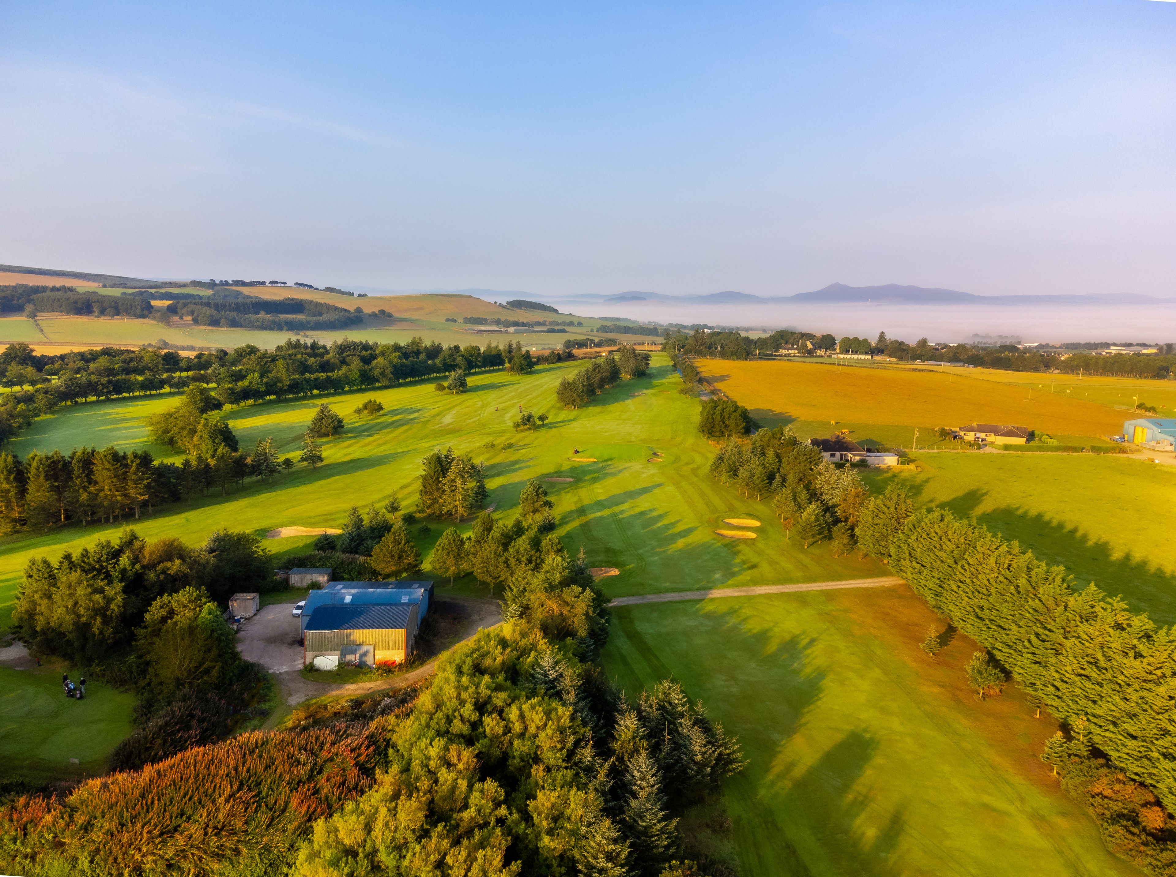 A golf course with a clubhouse, rolling hills, and a distant mountain range.