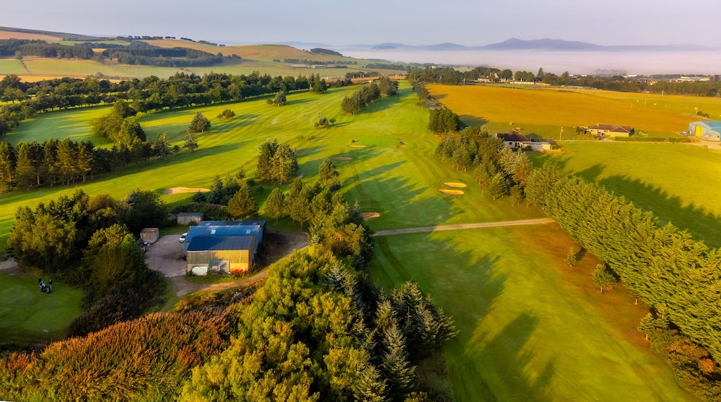 A golf course with a clubhouse, rolling hills, and a distant mountain range.