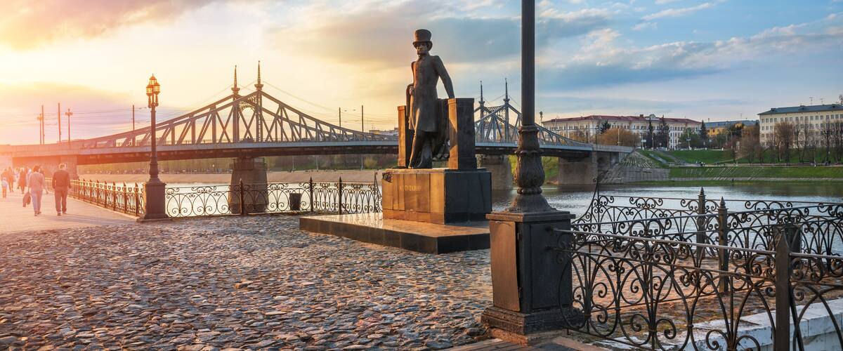 A statue on a waterfront promenade with a bridge in the background.