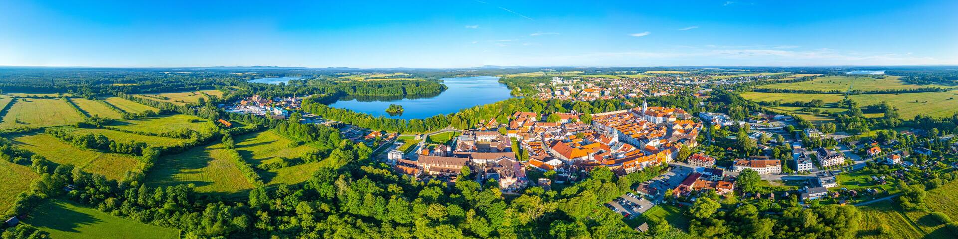 A town with a lake surrounded by green fields and a church with a tall spire.