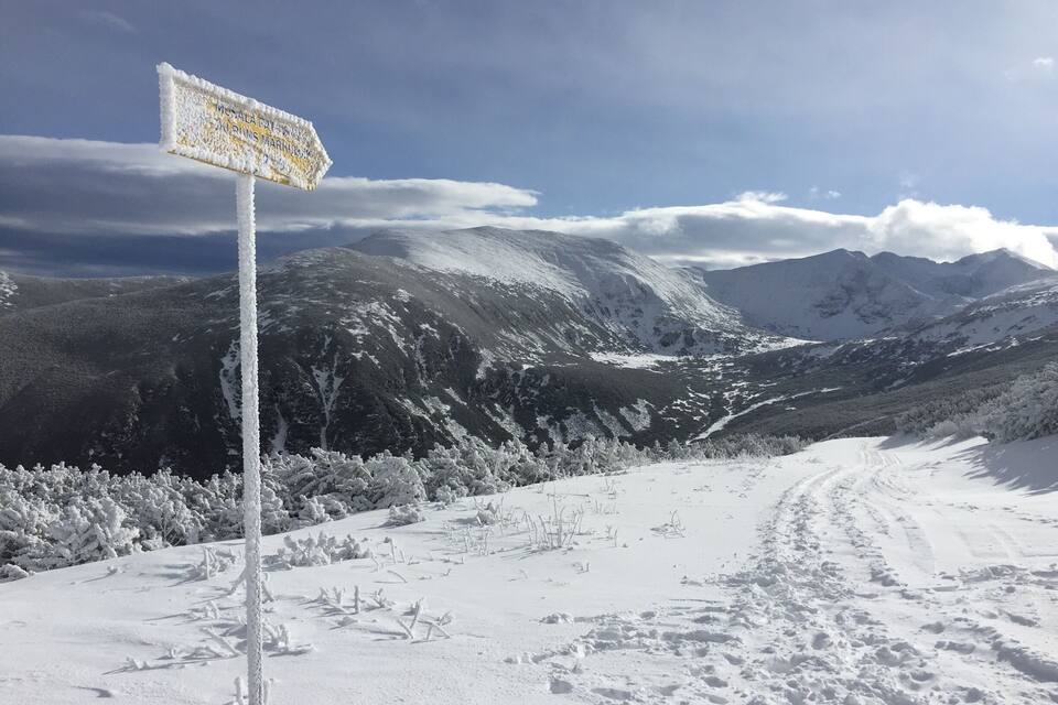 Paisaje montañoso cubierto de nieve con un indicador señalando direcciones.