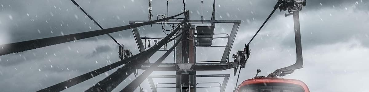 A red cable car suspended by cables against a cloudy sky.