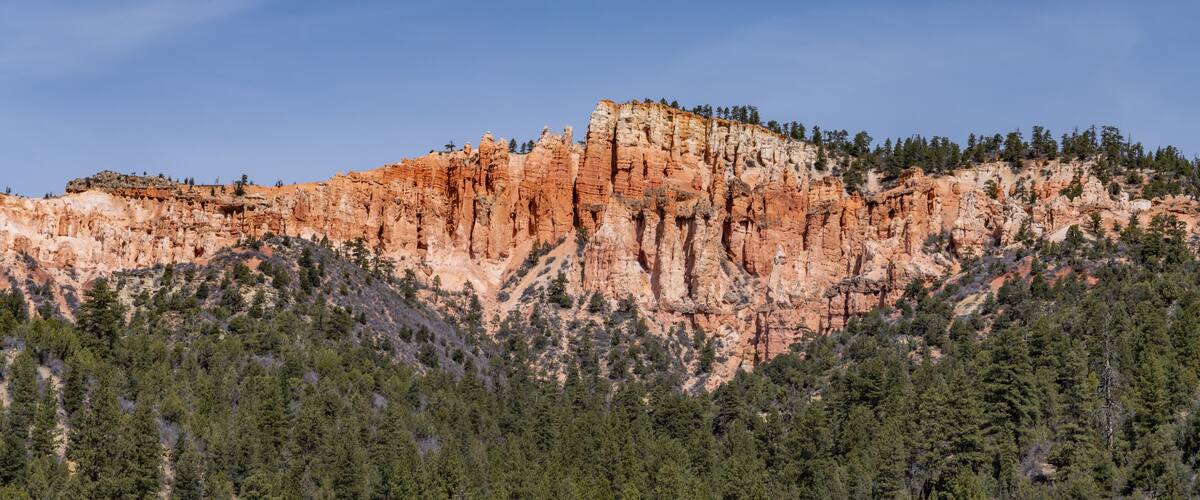 A rugged mountain with reddish-brown rock formations and dense green forests at its base.