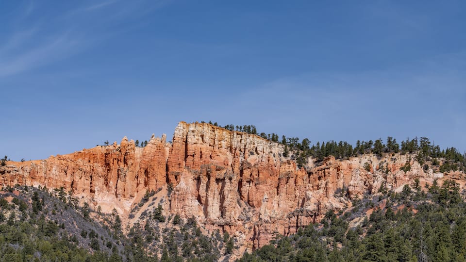 A rugged mountain with red rock formations and a forested base.