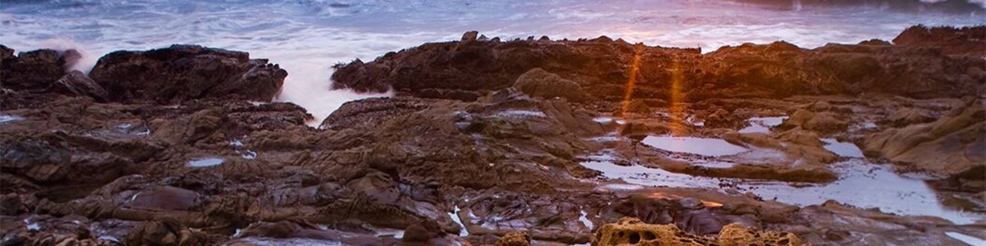 A rocky shoreline at sunset with the sun setting over the ocean.