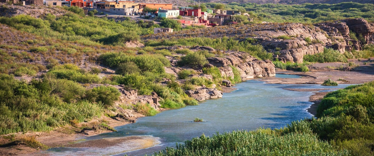 A river flowing through a hilly area with colorful buildings and sparse vegetation.