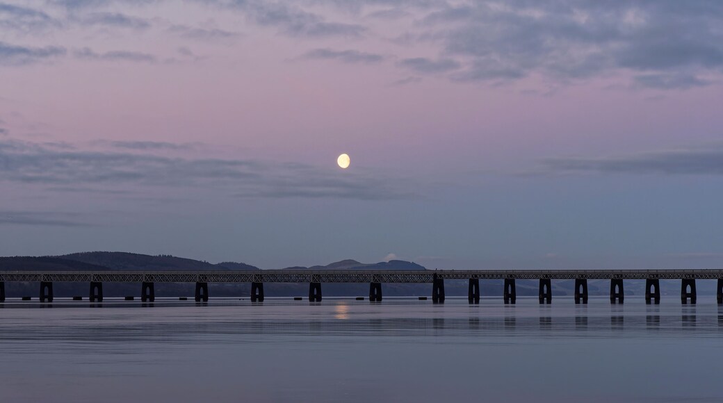 A bridge over calm water with a full moon in the sky.