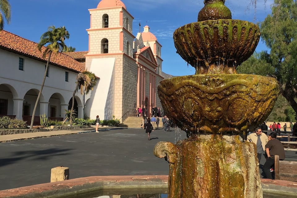 A historic church with a bell tower and a fountain in the foreground.