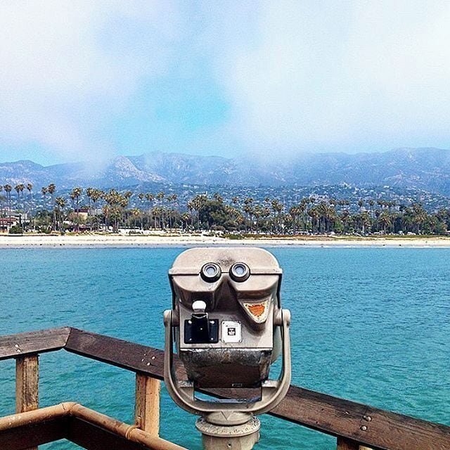 A pair of binoculars overlooking a coastal city with mountains in the background.