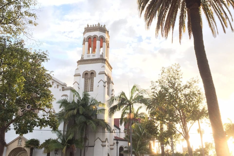 Uma igreja com um campanário e palmeiras ao primeiro plano.