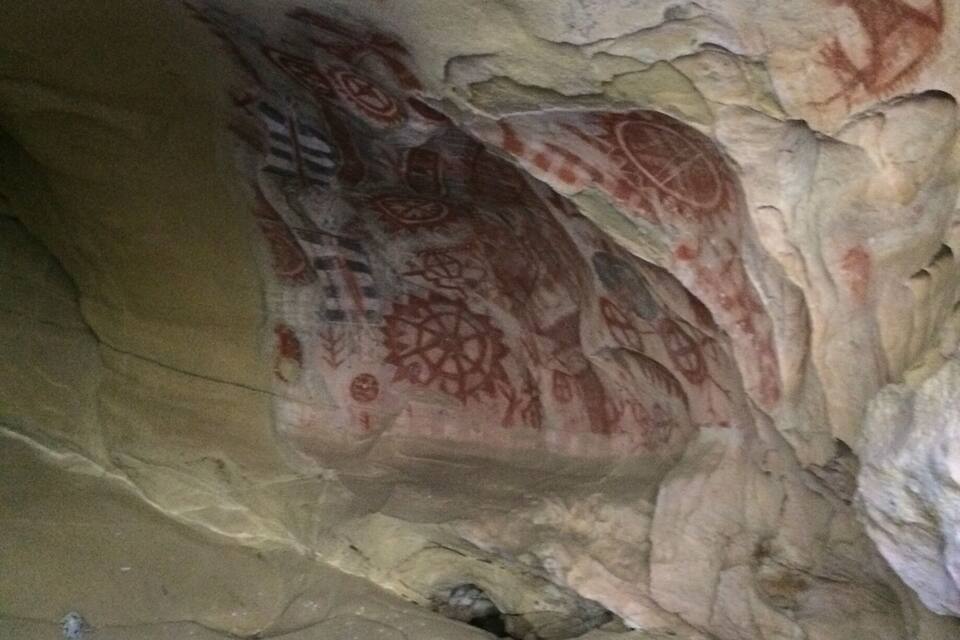 A cave interior with ancient red and white petroglyphs on the walls.