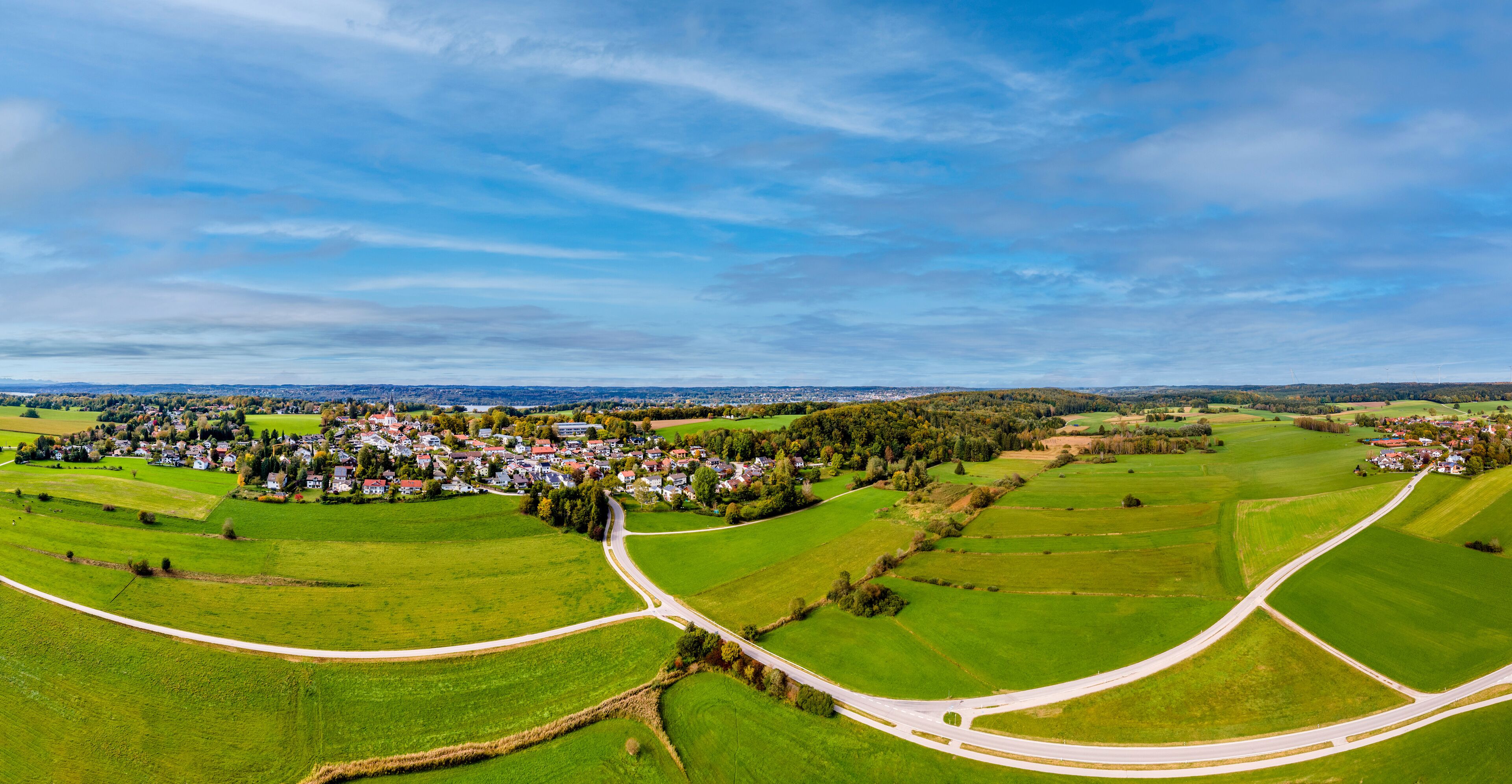 A rural landscape with a winding road, green fields, and a small village.
