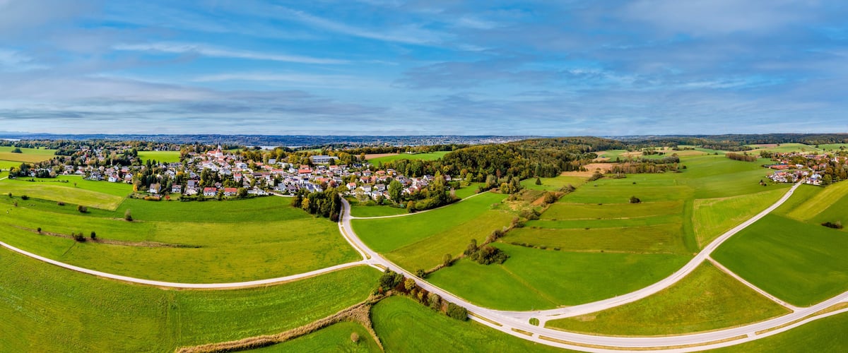 A rural landscape with a winding road, green fields, and a small village.