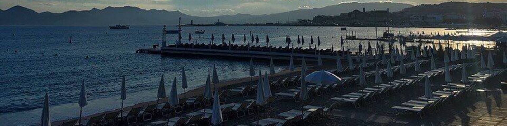 Un atardecer costero con un muelle que se adentra en el mar, rodeado de sombrillas y sillas de playa.
