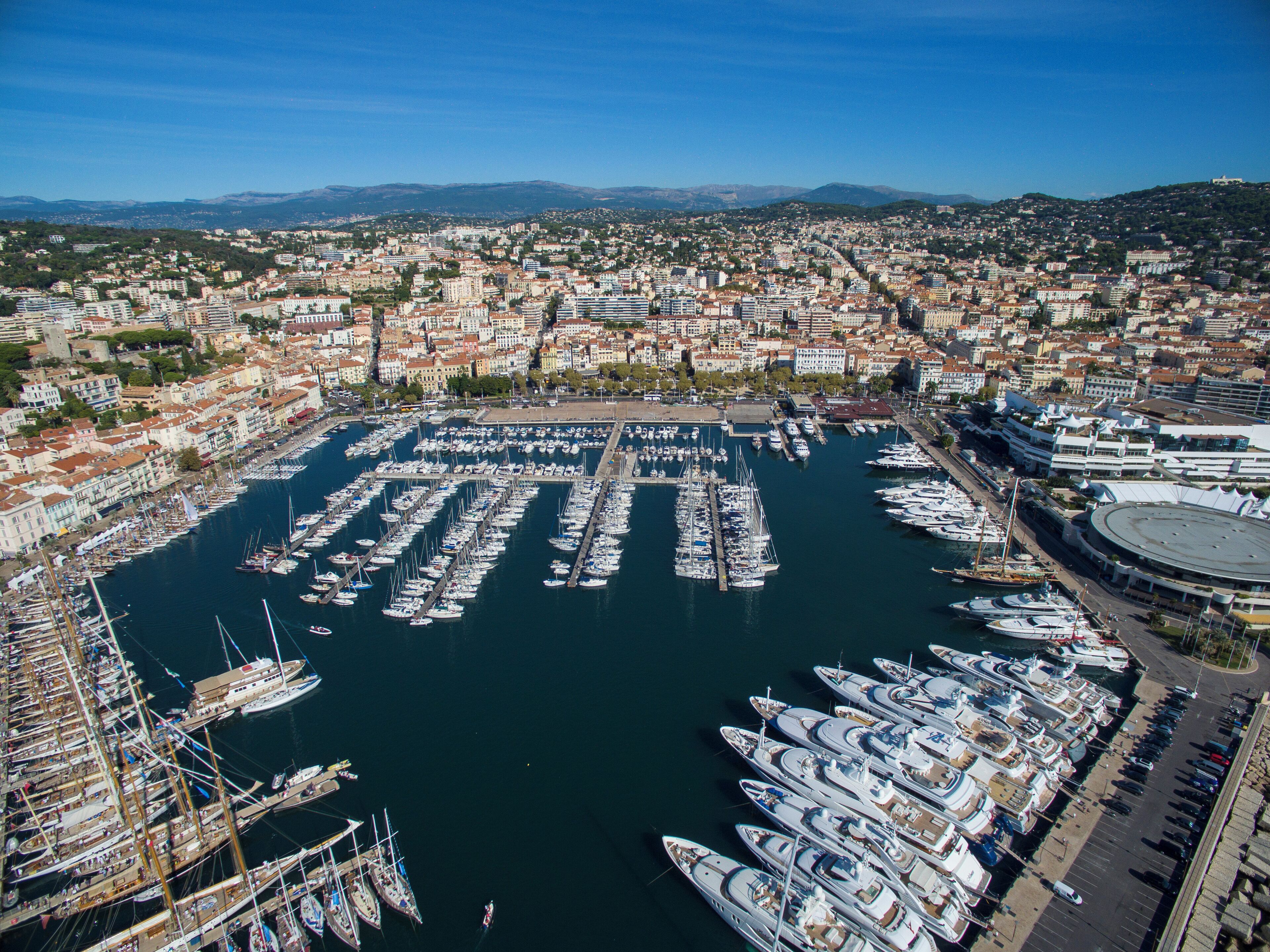 A marina filled with boats, a cityscape in the background, and mountains in the distance.