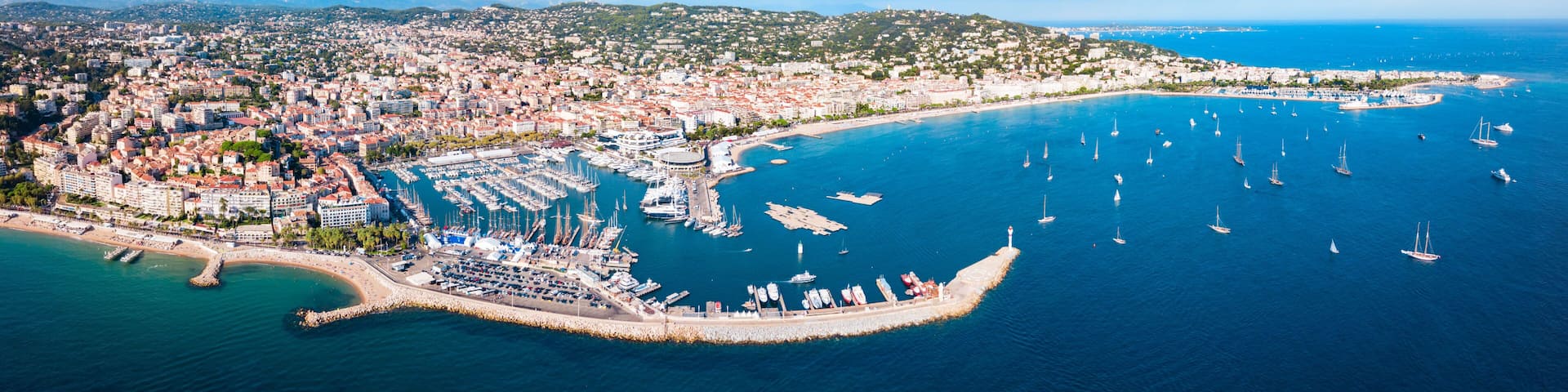 A coastal cityscape with a marina, boats, and a hilly backdrop.