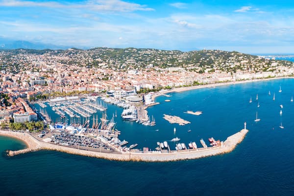 Un paysage urbain côtier avec un port de plaisance, des bateaux et une chaîne de collines en arrière-plan.
